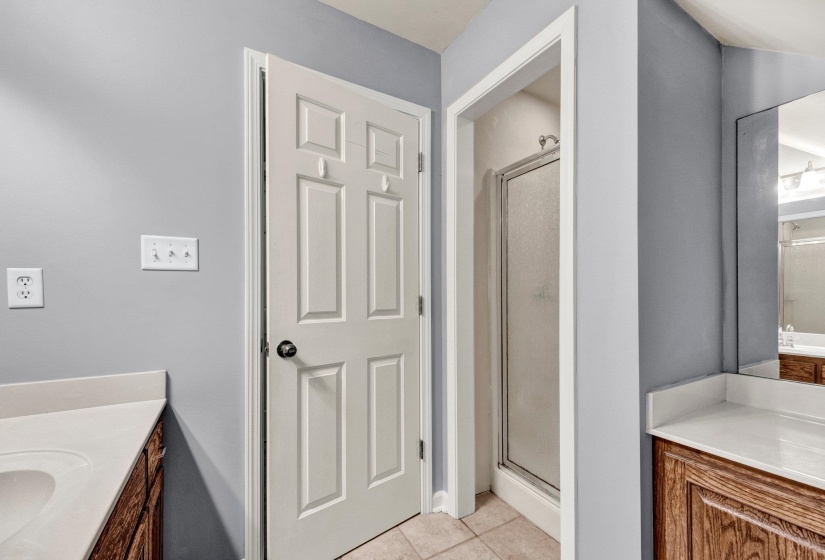 Bathroom featuring a glass-enclosed shower, light-toned tile flooring, and a vanity with a light countertop and wood-finish cabinetry