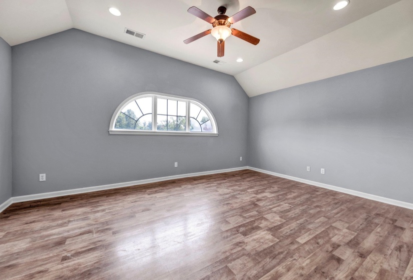 Spacious room featuring a prominent arched window, vaulted ceiling, wood-finish flooring, recessed lighting, and a ceiling fan