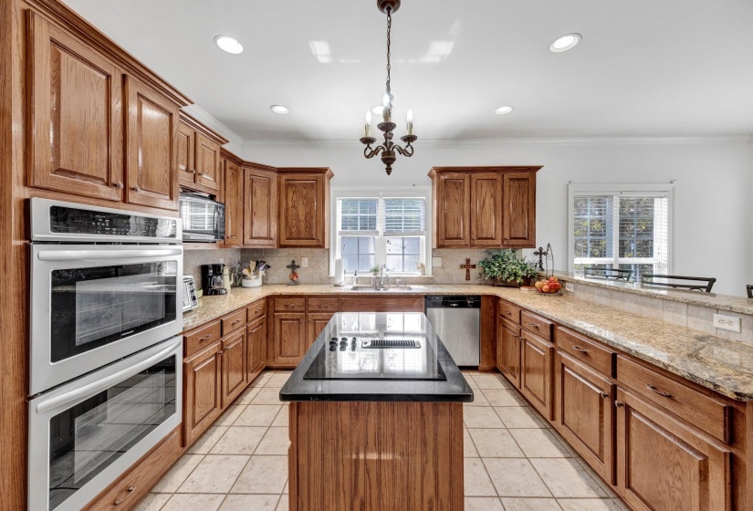 Spacious kitchen featuring extensive wood cabinetry, granite countertops, and a central island with an integrated cooktop