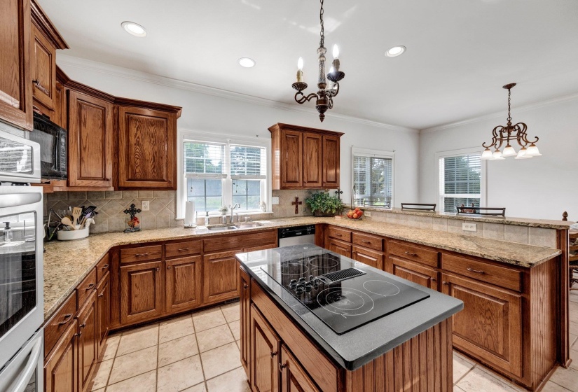 Kitchen featuring a central island with a built-in cooktop, extensive wood cabinetry, light-toned countertops, and tile flooring