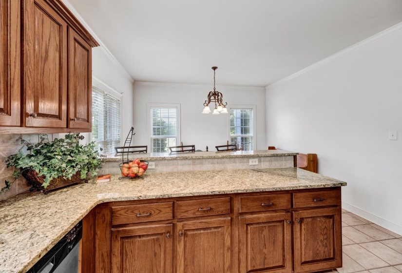 Kitchen featuring wood cabinetry, light-toned granite countertops, a tiled backsplash, and tiled flooring