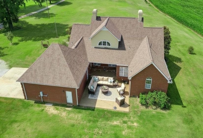 Brick exterior residence featuring a multi-gabled roofline, a rear patio with concrete and paver sections, a dormer window, and an expansive surrounding lawn