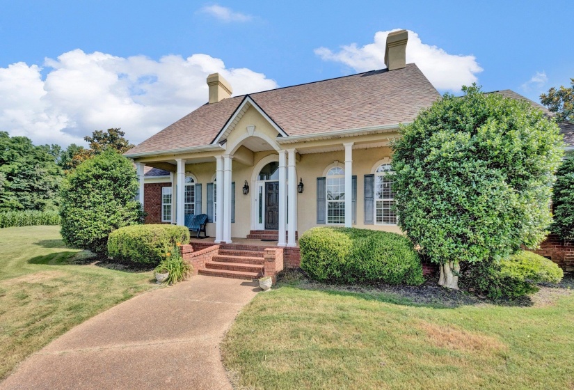 Stucco and brick exterior featuring a covered front porch with white columns, arched entry, brick steps, and a paved walkway