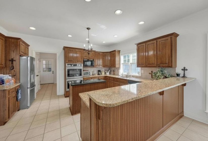 Spacious kitchen featuring warm wood cabinetry, granite countertops, tile flooring, built-in double ovens, and recessed lighting