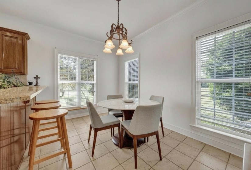 Kitchen dining area featuring neutral tile flooring, multiple windows with blinds, and crown molding