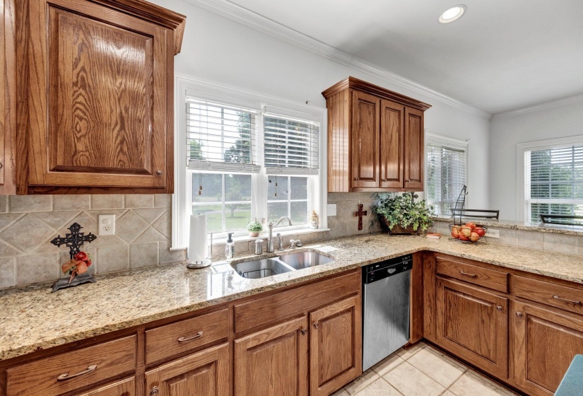 Kitchen featuring wood cabinetry, light-toned countertops, a tile backsplash, and a stainless steel dishwasher