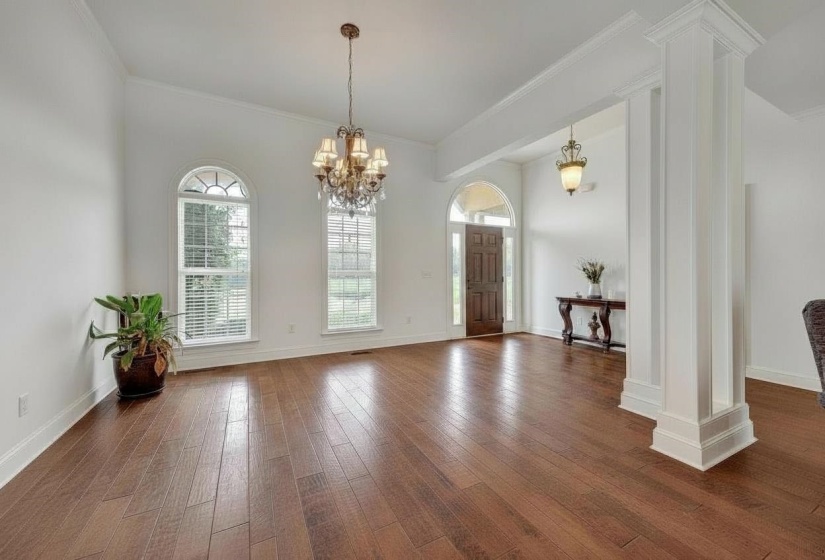 Expansive entry hall featuring rich wood-finish flooring, a decorative chandelier, and tall arched windows with blinds