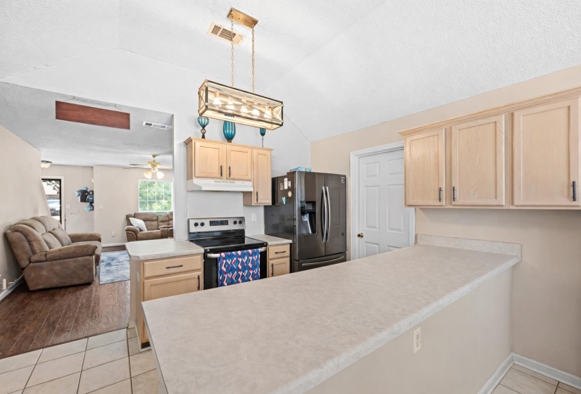 Kitchen featuring light wood-finish cabinetry, a black range, a black refrigerator, and an eat-at counter with a light-toned surface