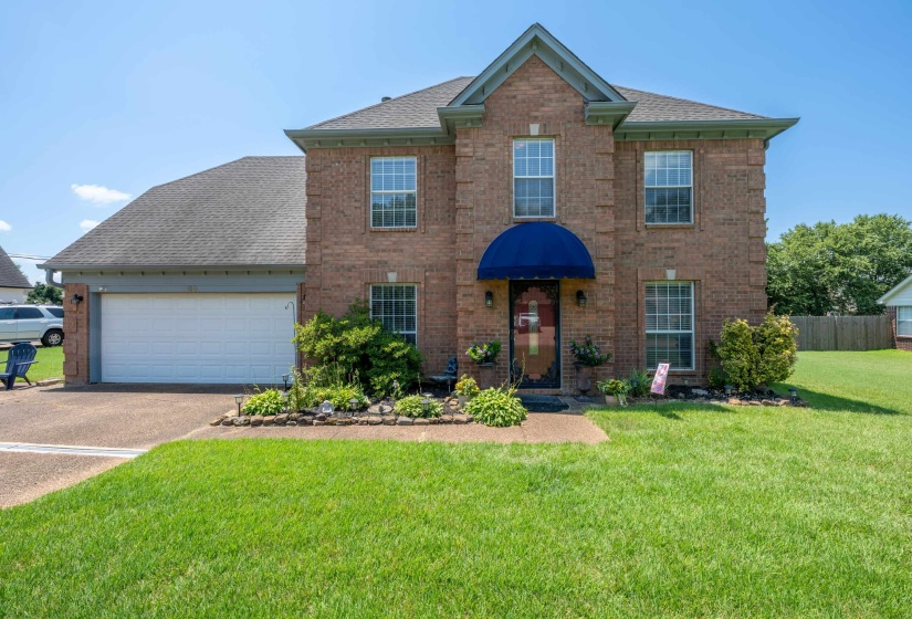 Brick facade residence featuring a two-car garage, established landscaping, and a front entry with a prominent blue awning