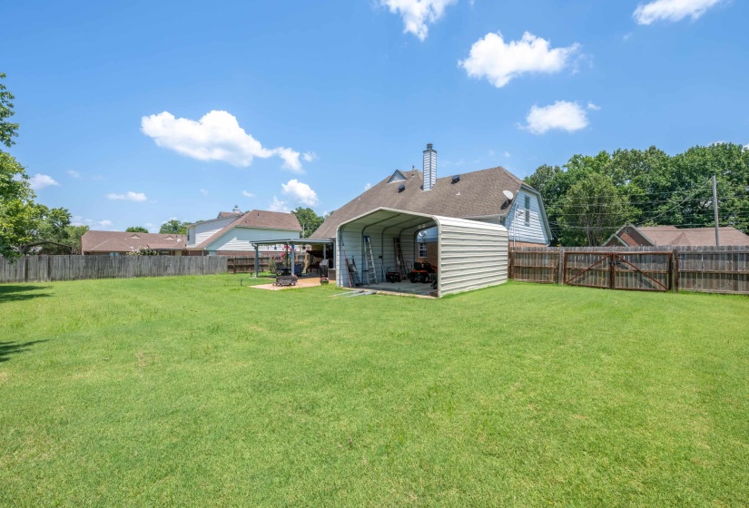 Spacious backyard featuring a large green lawn, full wood privacy fencing, and a metal carport structure