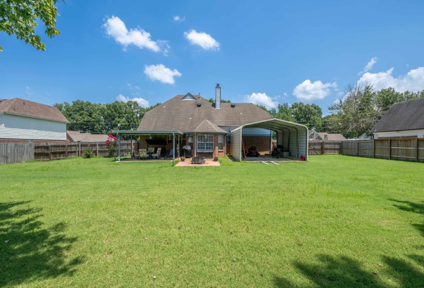 Spacious backyard featuring a covered patio, extensive lawn, and a large detached carport