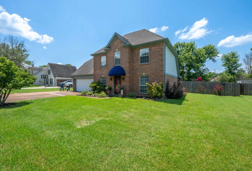 Brick exterior featuring a two-car garage, mature landscaping, and a fenced backyard
