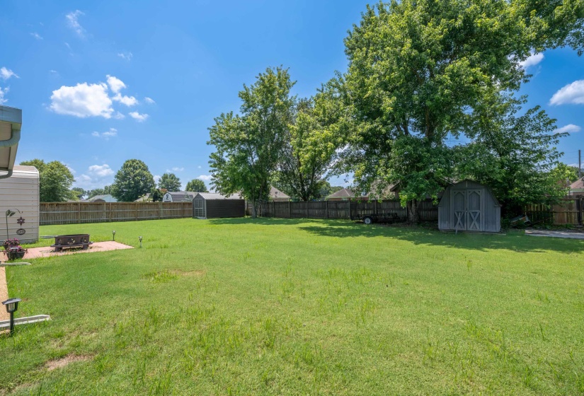 Expansive lawn area featuring a wooden privacy fence, two storage sheds, and mature trees