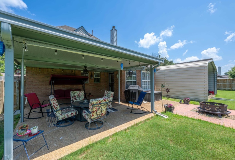 Covered patio with string lighting, brick exterior, metal storage structure, and a fenced yard