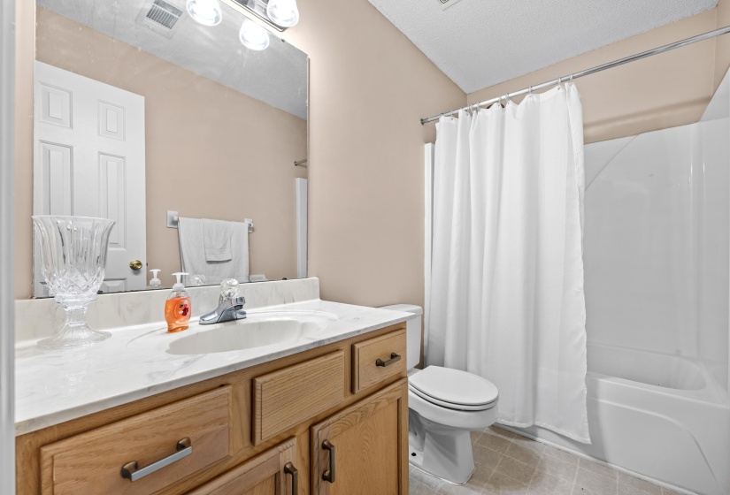 Bathroom featuring a light wood-finish vanity with a white countertop and integrated sink, a large wall-mounted mirror, a bath-shower combination with a white surround, and light-toned flooring