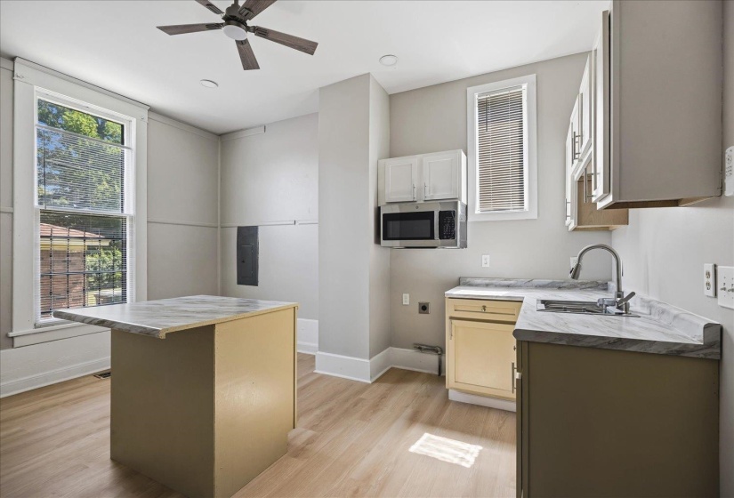 Kitchenette featuring wood-finish flooring, a ceiling fan, dual windows, built-in microwave, and a counter with an integrated sink