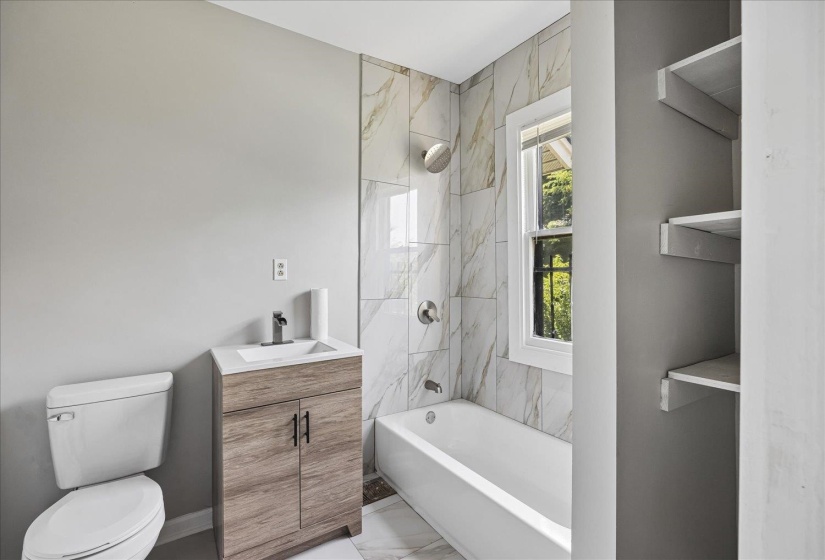 Bathroom with a white bathtub, a single-sink vanity with wood-finish cabinetry, and built-in shelving
