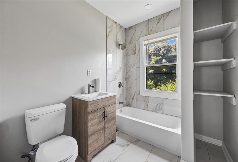 Bathroom featuring a white bathtub, a single pane window, and built-in shelving