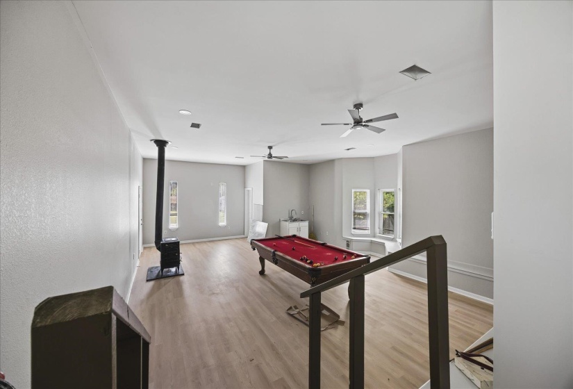 Spacious room featuring wood-finish flooring, a freestanding wood-burning stove, recessed lighting, and dual ceiling fans