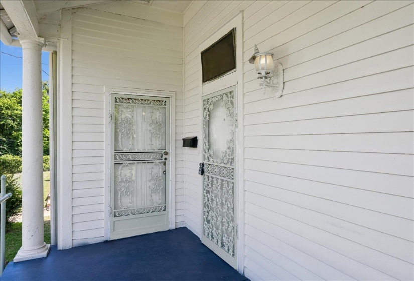 White clapboard siding exterior featuring a columned porch, two ornate screen doors, and a decorative wall-mounted light fixture