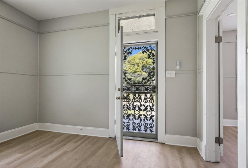 Interior room featuring light wood-finish flooring, light gray walls with decorative trim, and a prominent screen door with ornate black scrollwork