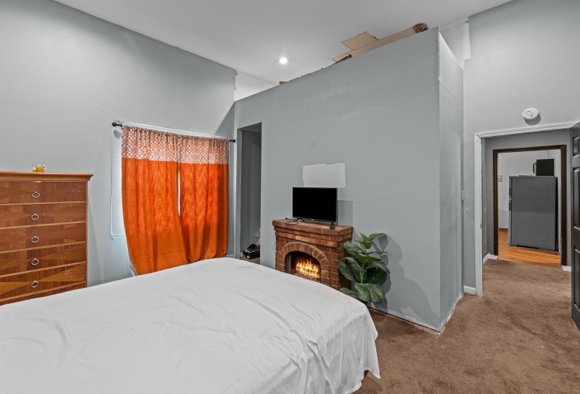 Bedroom featuring light gray walls, a window with orange drapes, and a partial brick-style fireplace structure