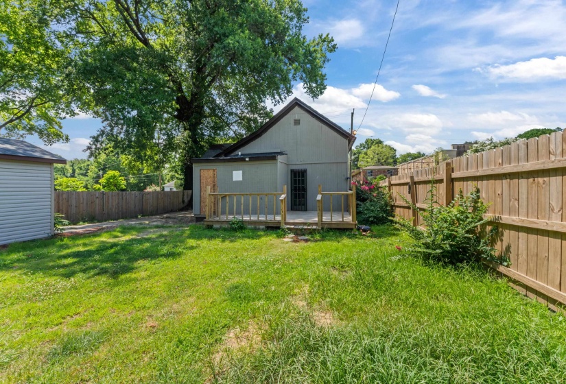 Expansive grassy backyard featuring a wooden privacy fence, a multi-level deck, a detached storage shed with siding, and mature trees