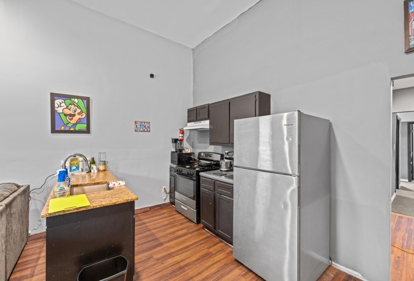 Compact kitchen featuring wood-finish flooring, dark cabinetry, and a granite-style countertop with an undermount sink