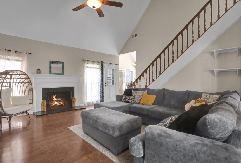 Living area with wood finished floors, ceiling fan, a fireplace, and vaulted ceiling