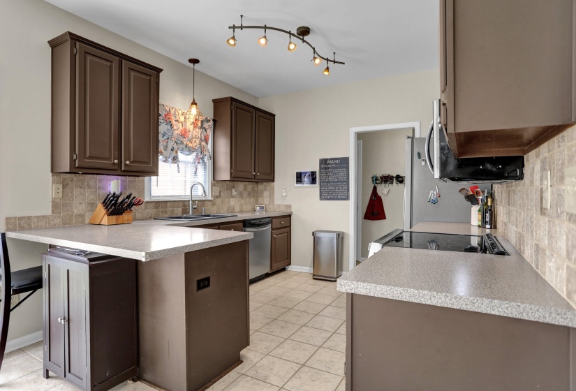 Kitchen with tasteful backsplash, dark wood finish cabinets, light countertops, and a peninsula