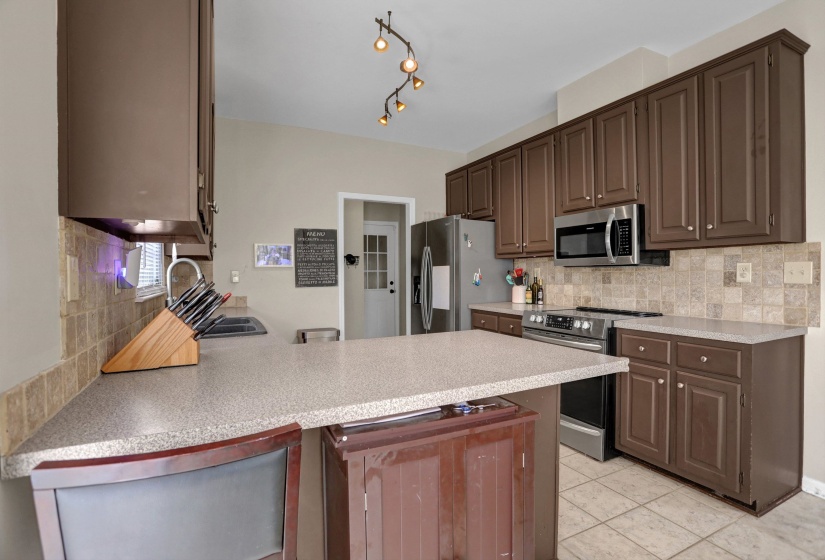 Kitchen with stainless steel appliances, a peninsula, backsplash, and light tile patterned floors