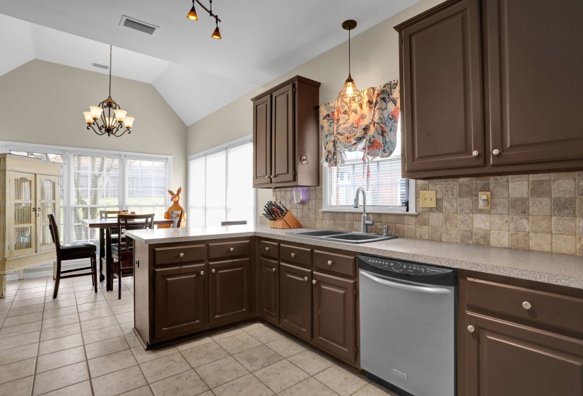 Kitchen with a peninsula, dark wood finish cabinetry, dishwasher, light countertops, and light tile patterned flooring