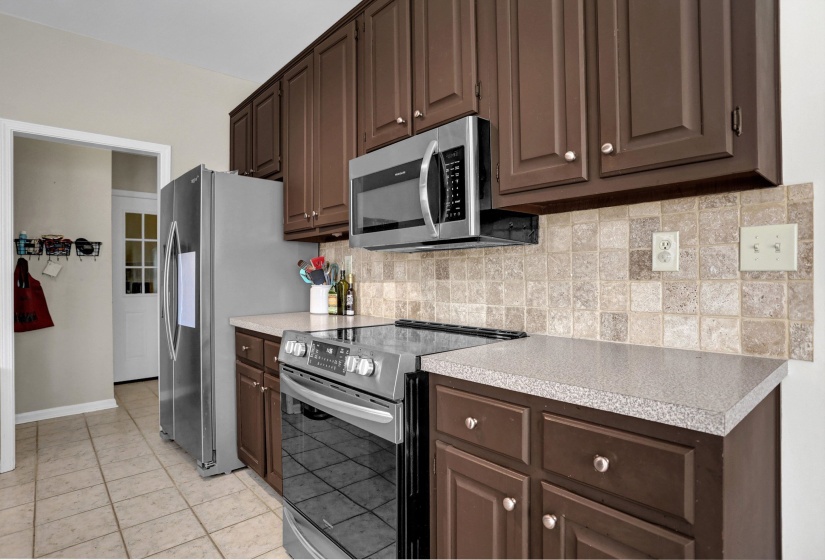 Kitchen with stainless steel appliances, light countertops, and dark wood finish cabinets