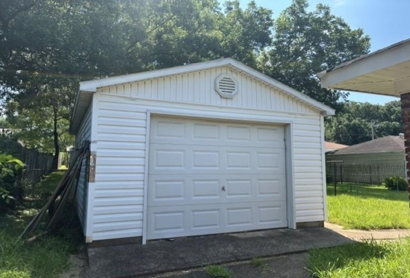 Detached garage featuring white vinyl siding and a paneled garage door
