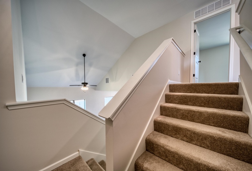 Stairs featuring ceiling fan, lofted ceiling, and carpet flooring
