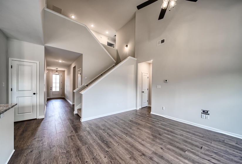 Empty room featuring a high ceiling, dark wood-style flooring, stairs, recessed lighting, and a ceiling fan