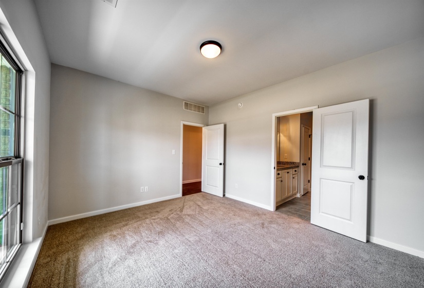 Unfurnished bedroom featuring ensuite bathroom and light carpet