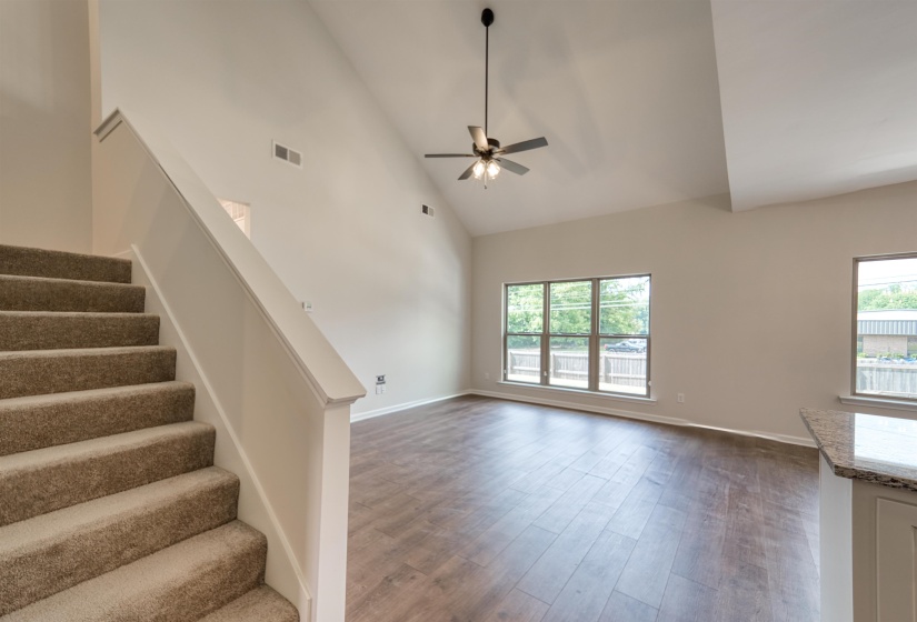 Unfurnished living room featuring high vaulted ceiling, dark wood finished floors, a ceiling fan, and stairs