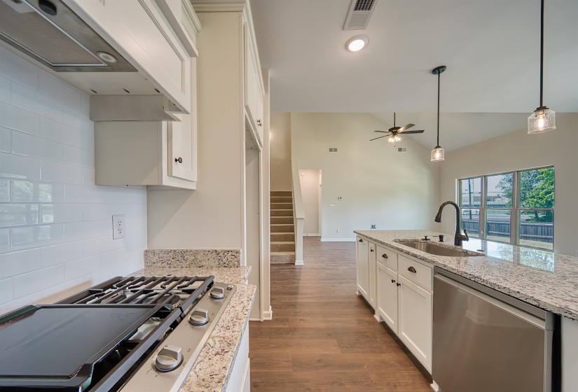 Kitchen featuring appliances with stainless steel finishes, vaulted ceiling, dark wood finished floors, white cabinetry, and light stone countertops