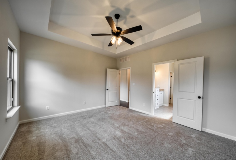Unfurnished bedroom with a tray ceiling, carpet, connected bathroom, and a ceiling fan
