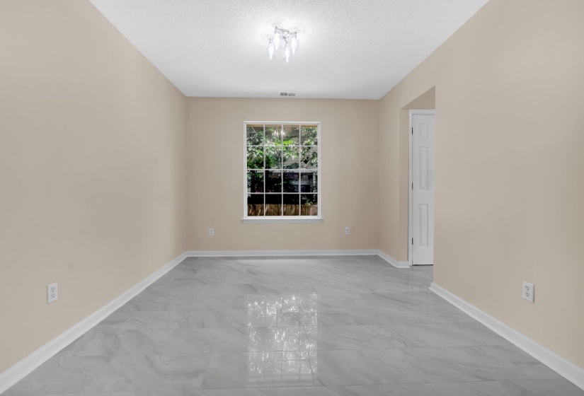 Spacious room featuring light-toned walls, a large window with exterior greenery, and sleek gray tile flooring