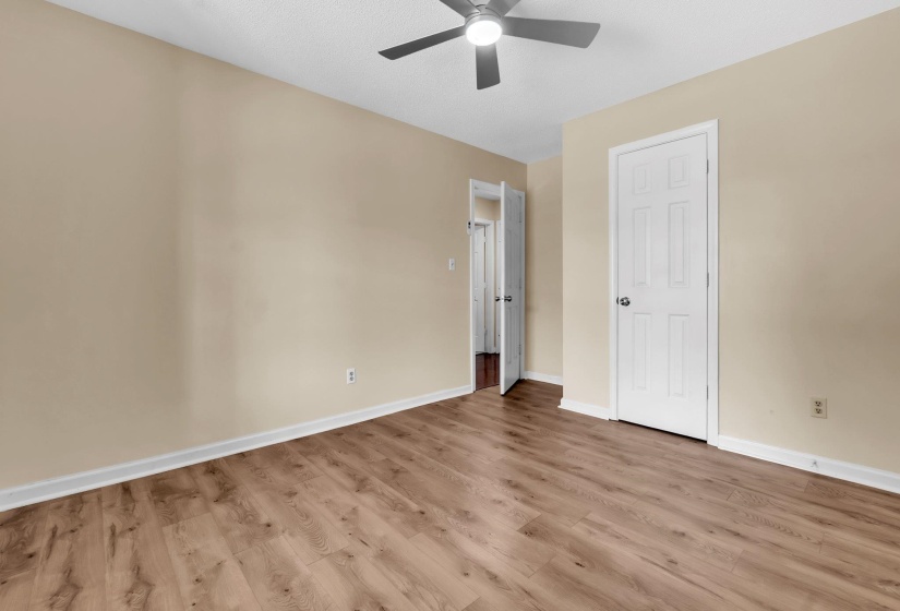 Interior room with wood-finish flooring, light beige walls, white baseboards, and a ceiling fan with integrated lighting