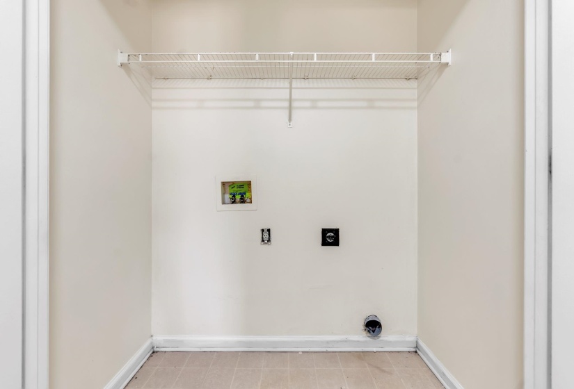 Dedicated laundry space featuring a wire shelf, light-toned wall paint, baseboard trim, and tile flooring