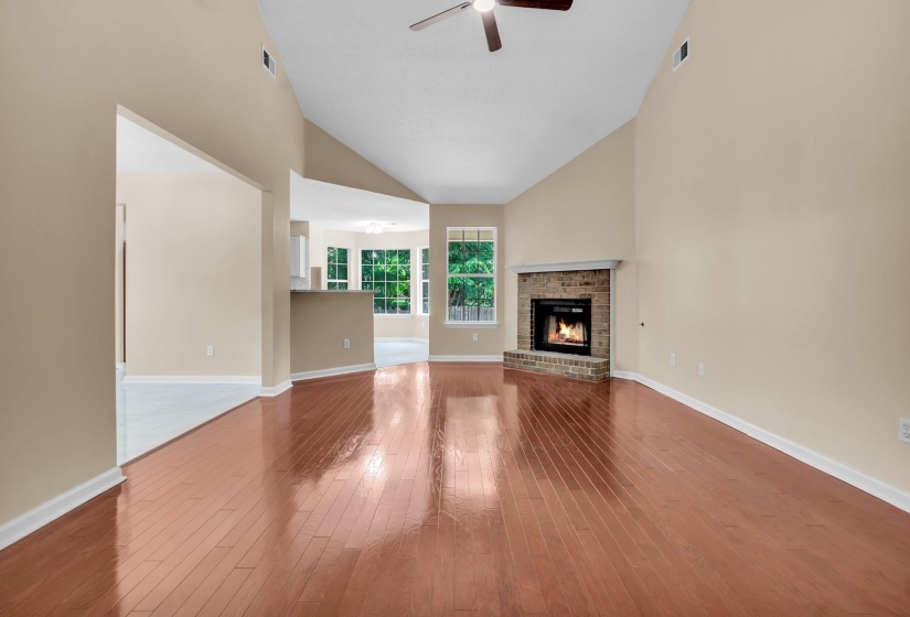 Spacious living area featuring high vaulted ceilings, warm wood-finish flooring, and a brick-surround fireplace