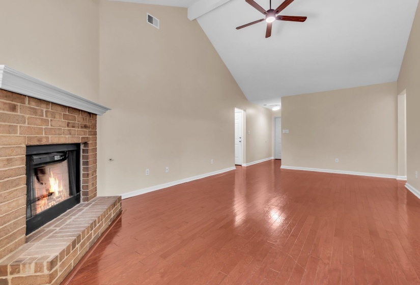 Living room featuring a brick fireplace with a white mantel, vaulted ceiling, wood-finish flooring, and a ceiling fan