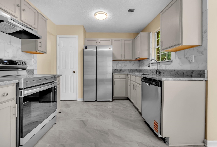 Kitchen featuring light-toned cabinetry, stainless steel appliances, marble-patterned backsplash, light gray countertops, and gray tile flooring