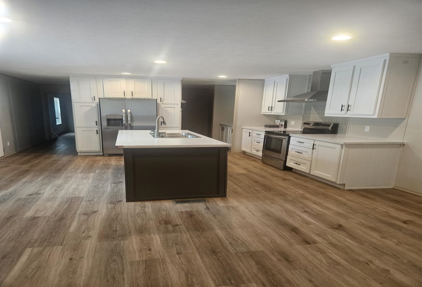 Modern kitchen featuring wood-finish flooring, white cabinetry, a dark-toned island with a stainless steel sink, stainless steel appliances, and recessed lighting