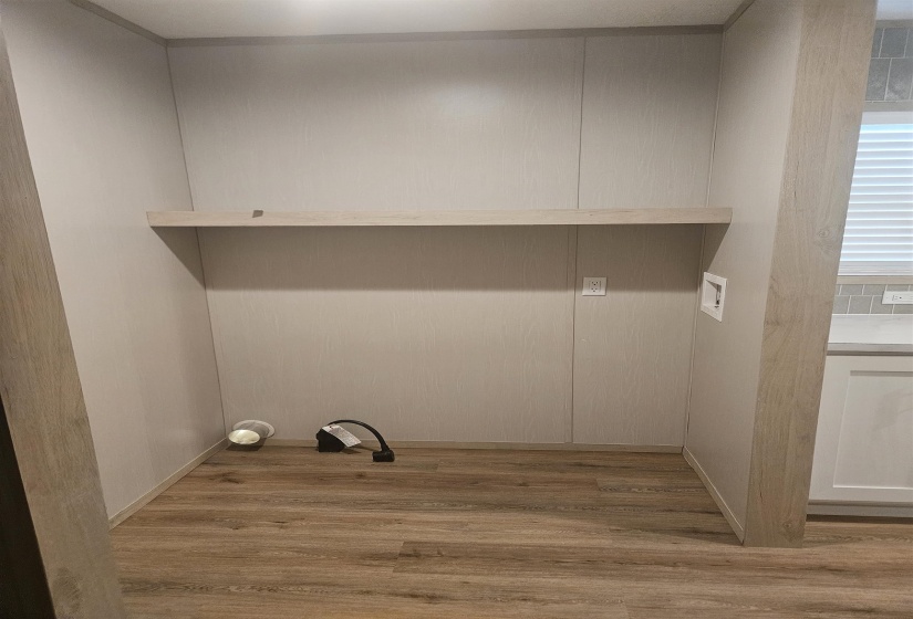 Dedicated laundry area featuring a built-in light wood-tone shelf, durable wood-finish flooring, and light-toned wall panels
