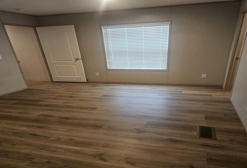 Wood-finish flooring throughout, featuring a window with horizontal blinds, neutral wall tones, and white trim
