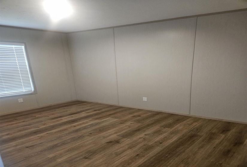 Room featuring wood-finish flooring, light-toned walls with paneling, baseboard trim, and a window with blinds